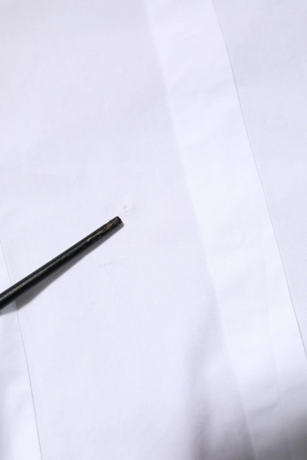 Un crayon noir mat élégant posé en diagonale sur une chemise homme dolce & gabbana en coton blanc à manches longues en or