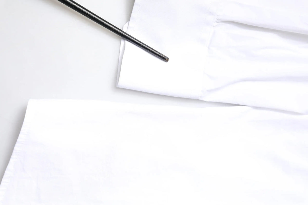 Un repose-baguettes en métal noir posé en diagonale sur un tissu blanc froissé d’une chemise homme en coton blanc dolce gabbana