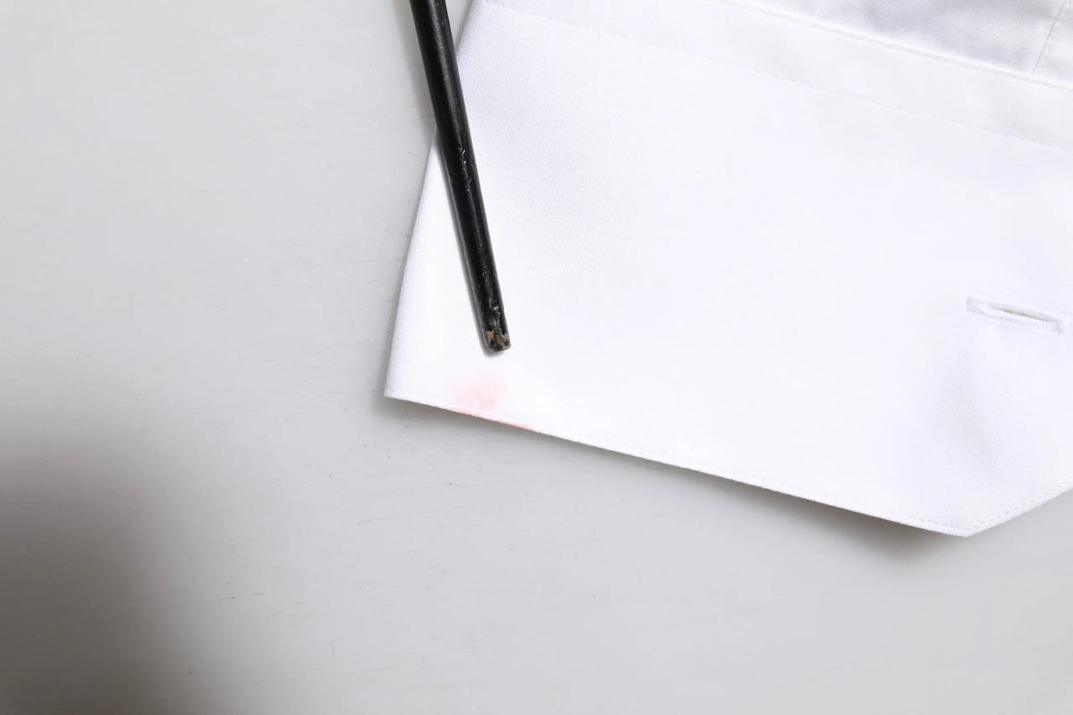 Stylo noir reposant sur papier blanc avec légère tache rose près de la pointe pour chemise blanche en or brodée dolce gabana