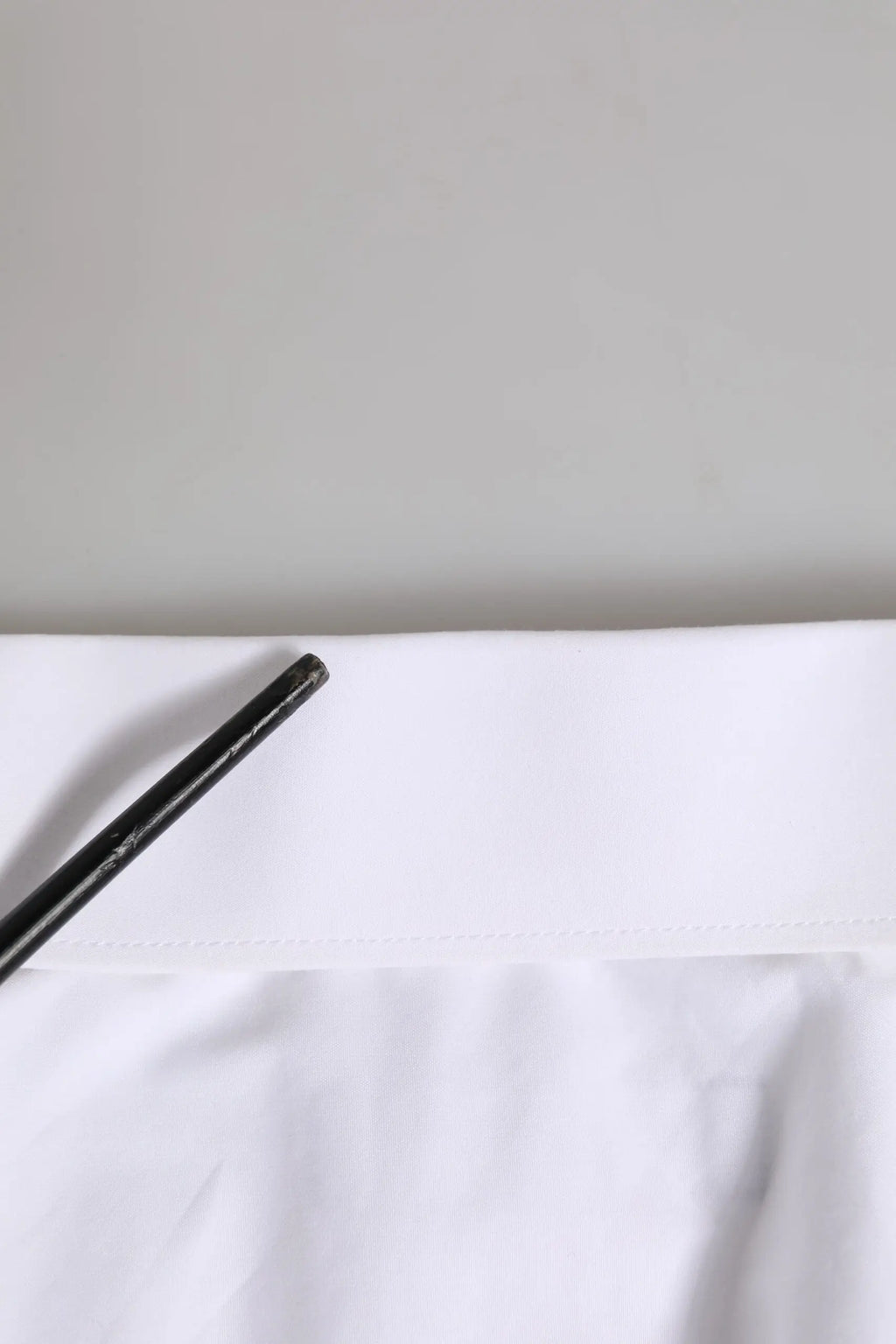 Un crayon noir élégant posé en diagonale sur un tissu blanc net du chemise formelle homme dolce & gabbana or blanc manches longues