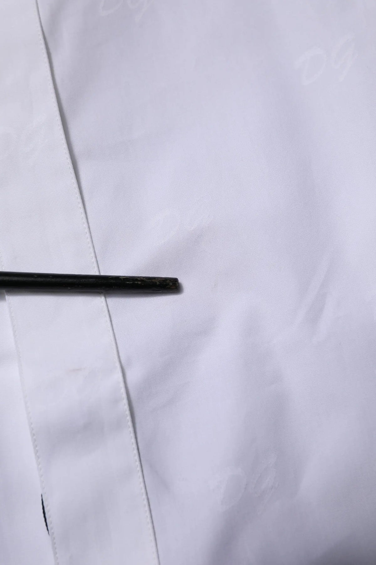 Objet cylindrique noir posé sur tissu blanc près d’une chemise formelle blanche en or Dolce & Gabbana à manches longues