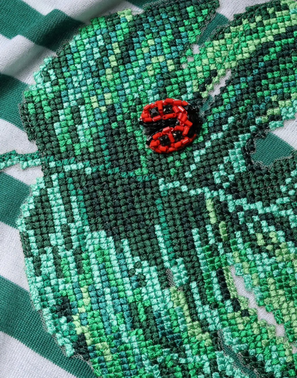 Broche coccinelle rouge et noire en perles sur un t shirt dolce gabbana blanc rayé vert à col rond avec motif feuille brodée