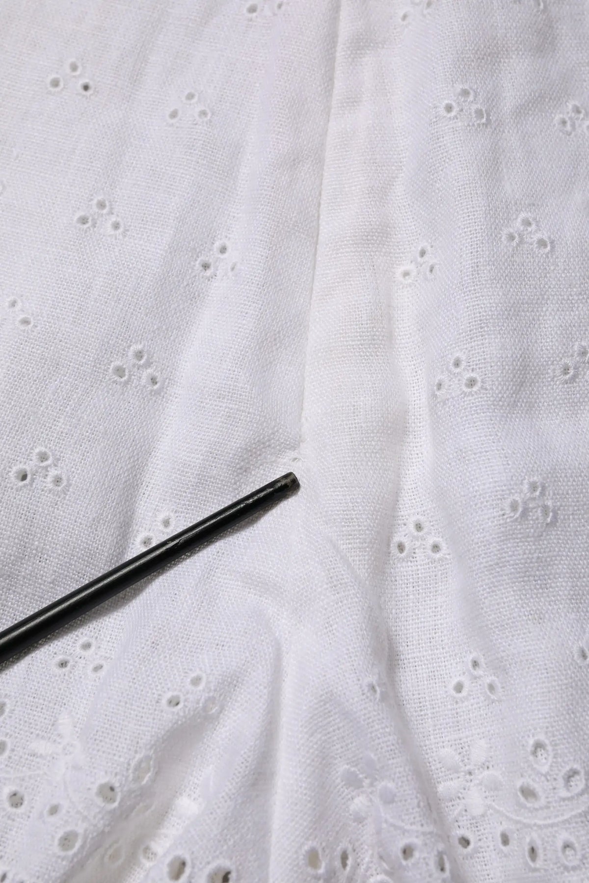 Un objet cylindrique noir posé sur un tissu blanc brodé avec un short blanc en lin taille haute dolce & gabbana