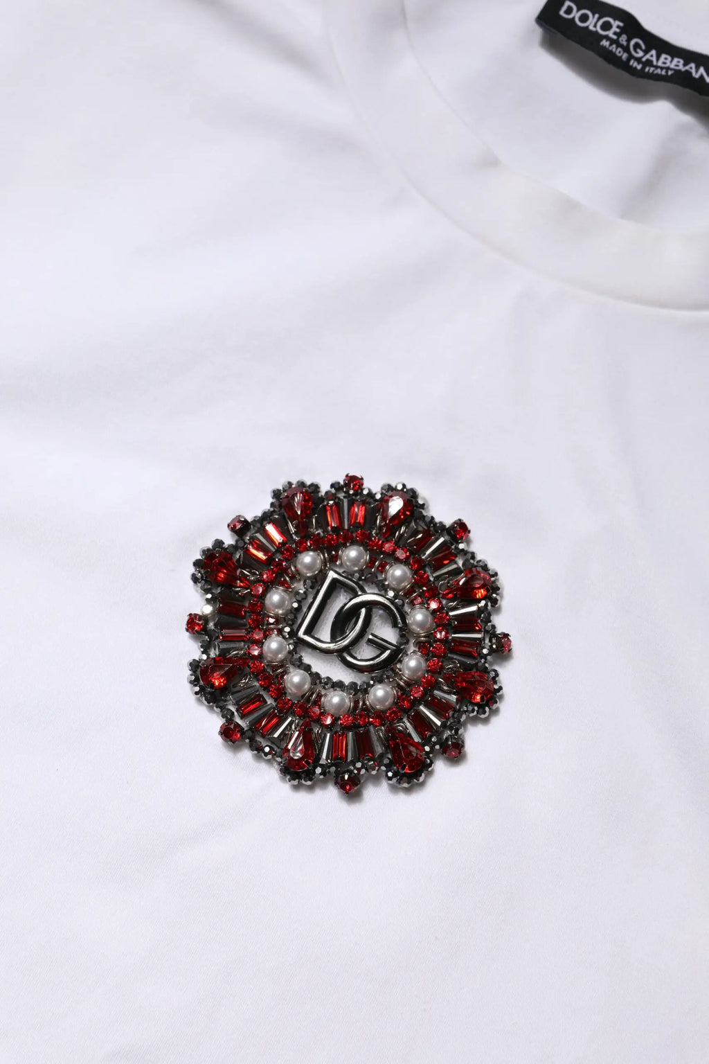Broche dolce gabbana rouge et argent avec logo dg central et pierres facettées sur t-shirt blanche manches courtes