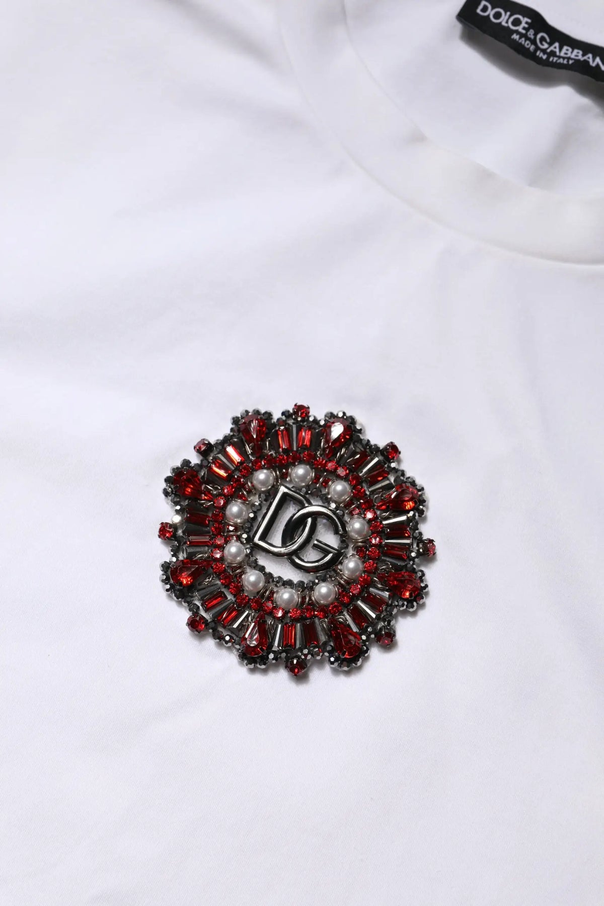 Broche dolce gabbana rouge et argent avec logo dg central et pierres facettées sur t-shirt blanche manches courtes