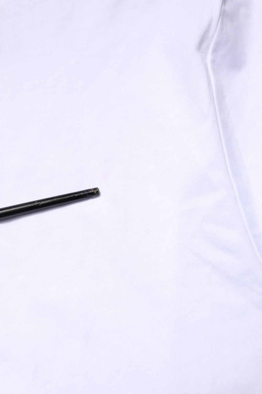 Objet cylindrique noir mat à côté d’un t-shirt dolce gabbana blanc avec broderie de logo sur le devant
