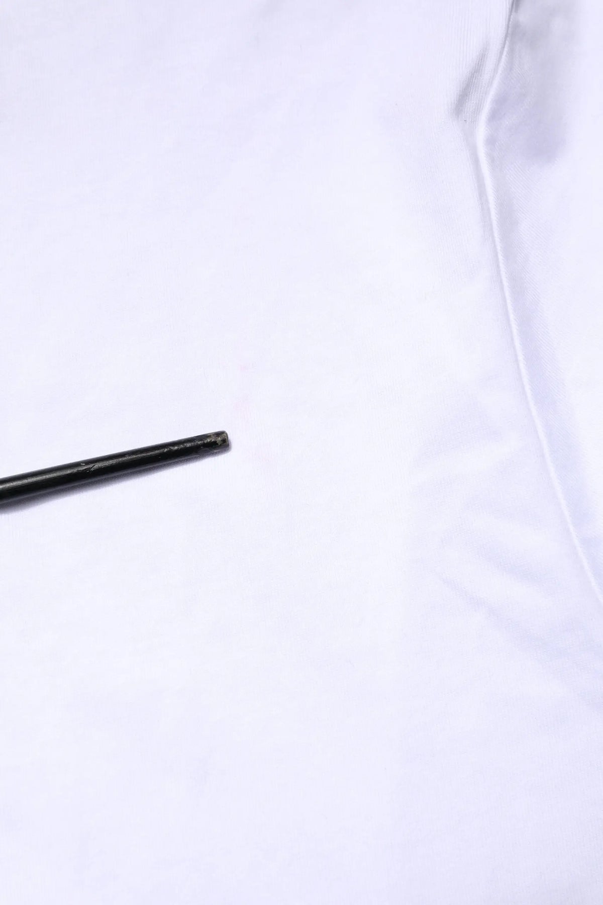 Objet cylindrique noir mat à côté d’un t-shirt dolce gabbana blanc avec broderie de logo sur le devant