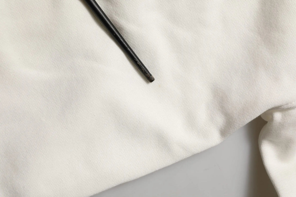 Crayon noir cylindrique posé sur tissu blanc à côté d’un sweat à capuche dolce & gabbana blanc avec logo