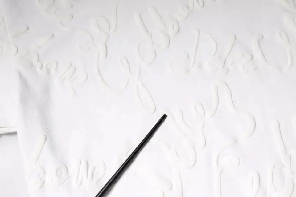 Objet cylindrique noir reposant sur une surface blanche texturée avec t shirt coton dolce & gabbana blanc imprimé logo