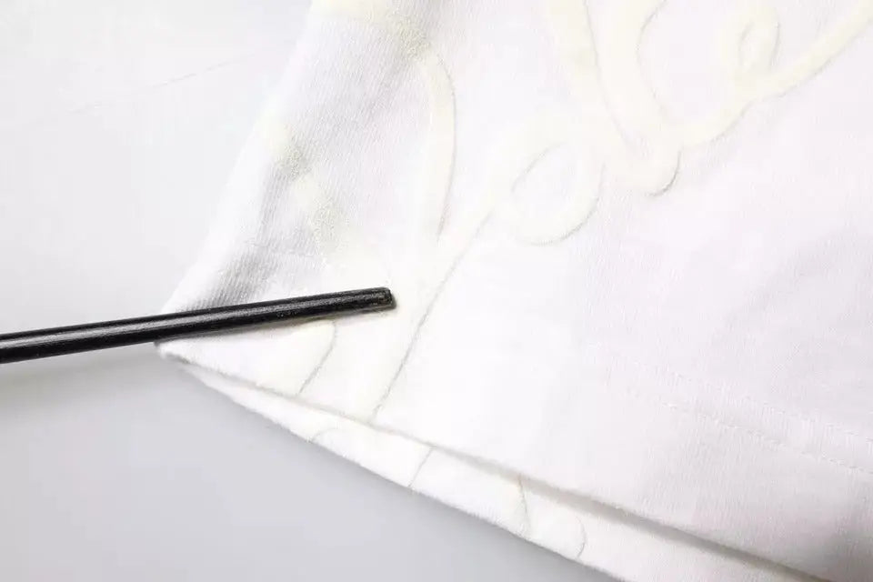 Une baguette noire reposant sur un tissu blanc avec broderie sur un t-shirt dolce & gabbana en coton blanc à logo imprimé