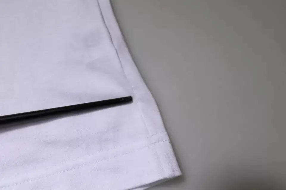 Un stylo noir élégant repose en diagonale sur l’ourlet soigneusement cousu d’un t-shirt blanc en coton dolce & gabbana panda king