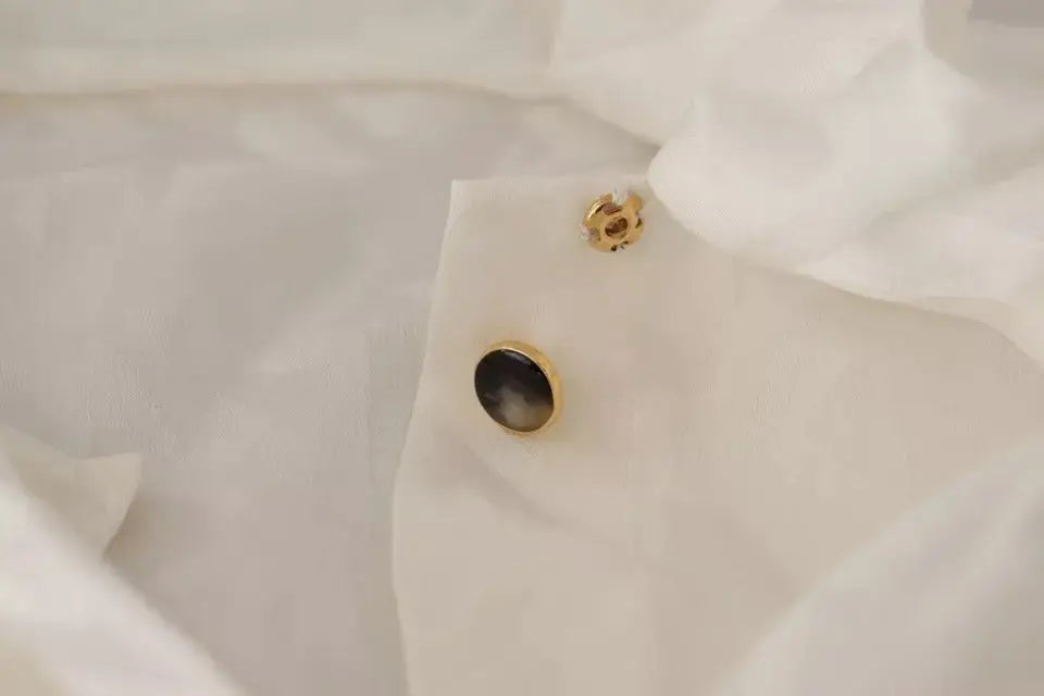 Bouton doré avec centre sombre circulaire sur manchette en tissu blanc du chemisier ascot en soie à motifs dolce & gabbana