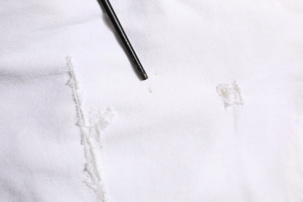 Un crayon noir posé en diagonale sur un tissu blanc à côté d un jean skinny déchiré en coton blanc dolce gabbana