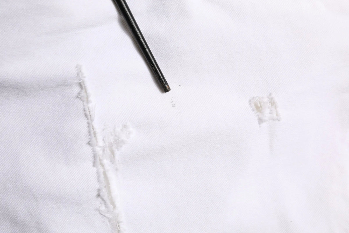 Un crayon noir posé en diagonale sur un tissu blanc à côté d un jean skinny déchiré en coton blanc dolce gabbana