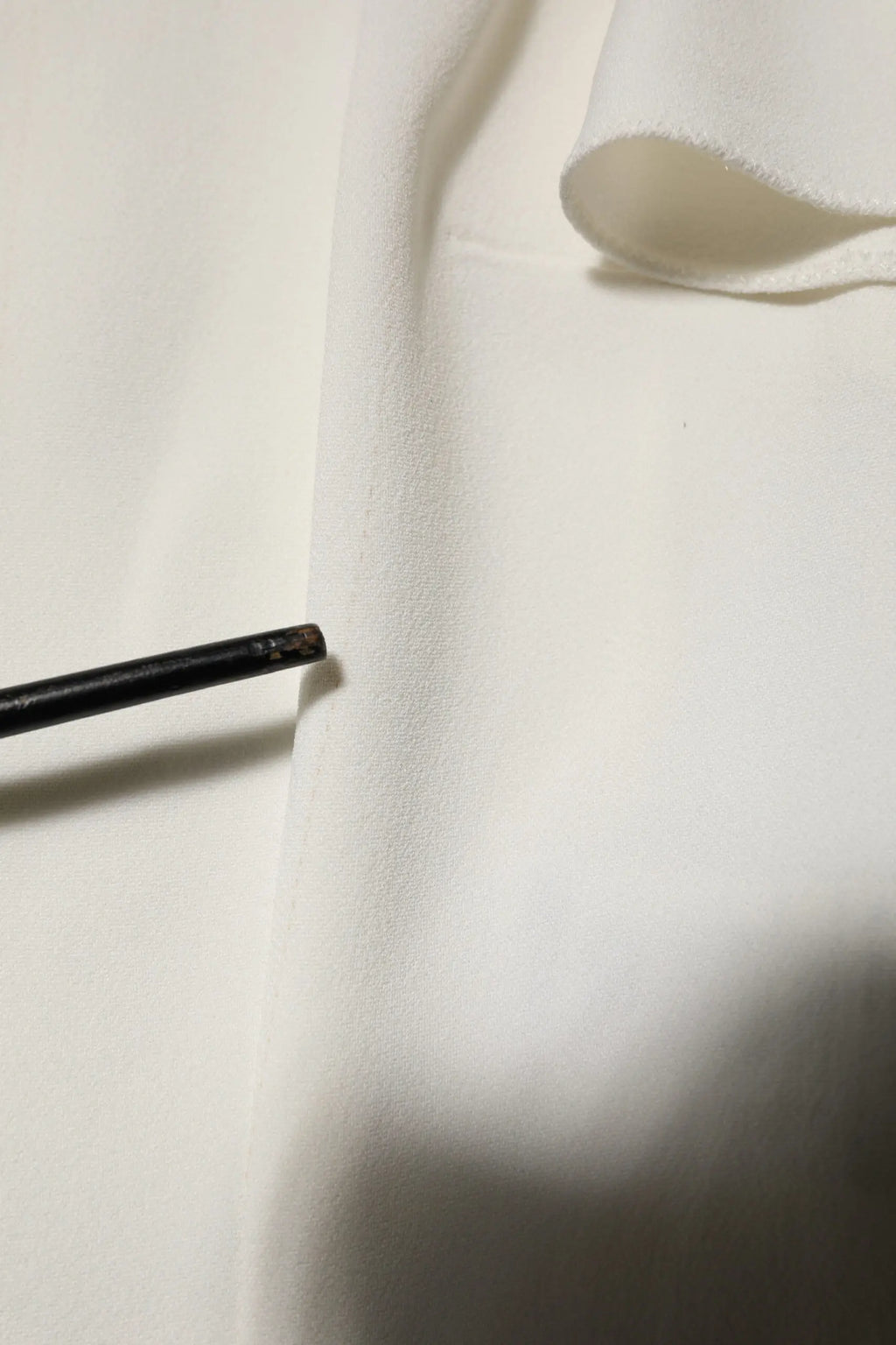 Objet cylindrique noir avec une extrémité usée appuyé sur un chemisier blanc dolce gabbana col rond manches courtes
