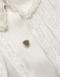Broche délicate en forme de fleur avec pierre dambre centrale et petites pierres claires en métal argenté sur blouse blanche en soie transparente à volants dolce gabbana