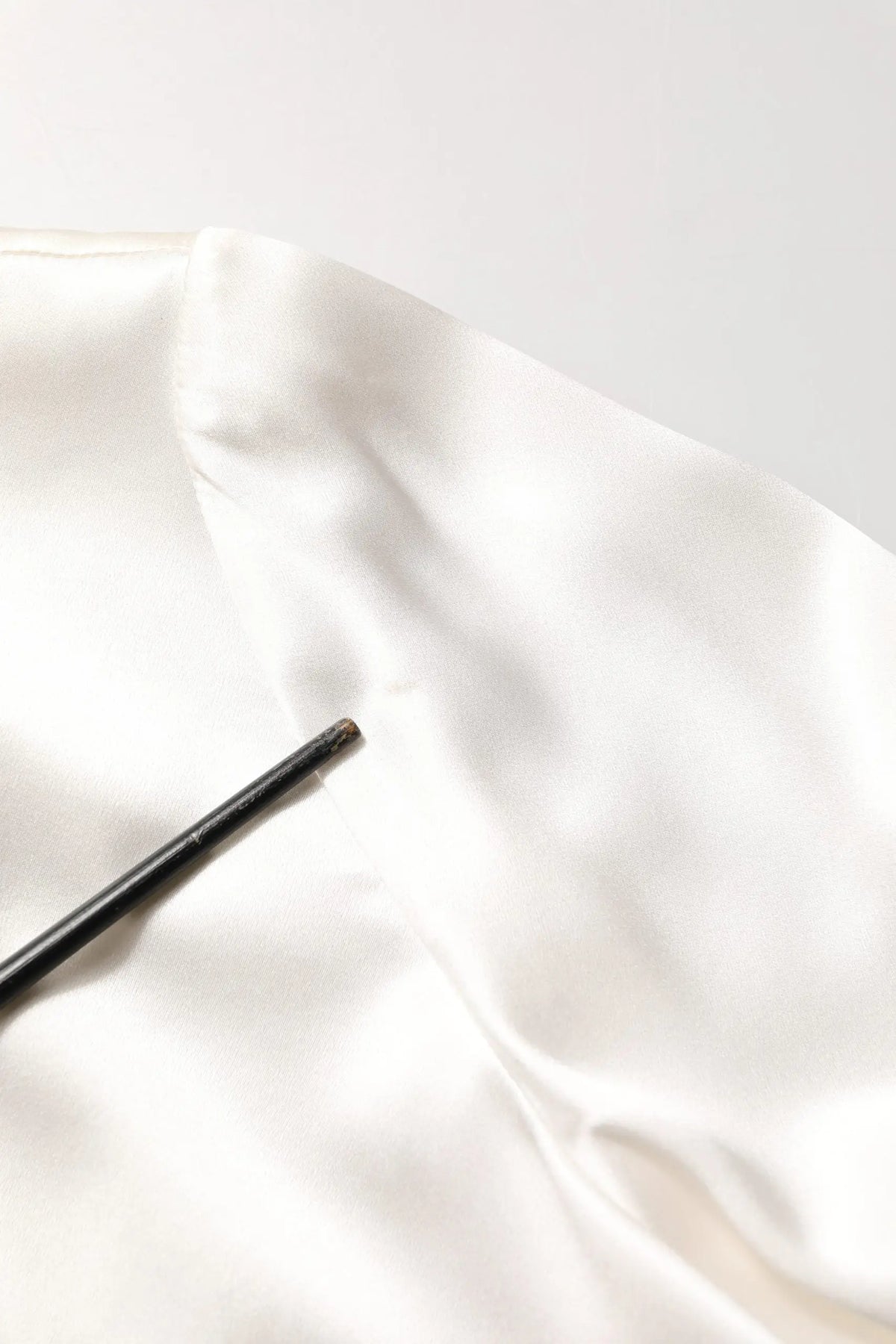 Une brosse noire élégante posée sur un tissu en soie blanche fluide à côté d’un chemisier blanc en satin dolce gabbana avec finitions en dentelle et manches longues