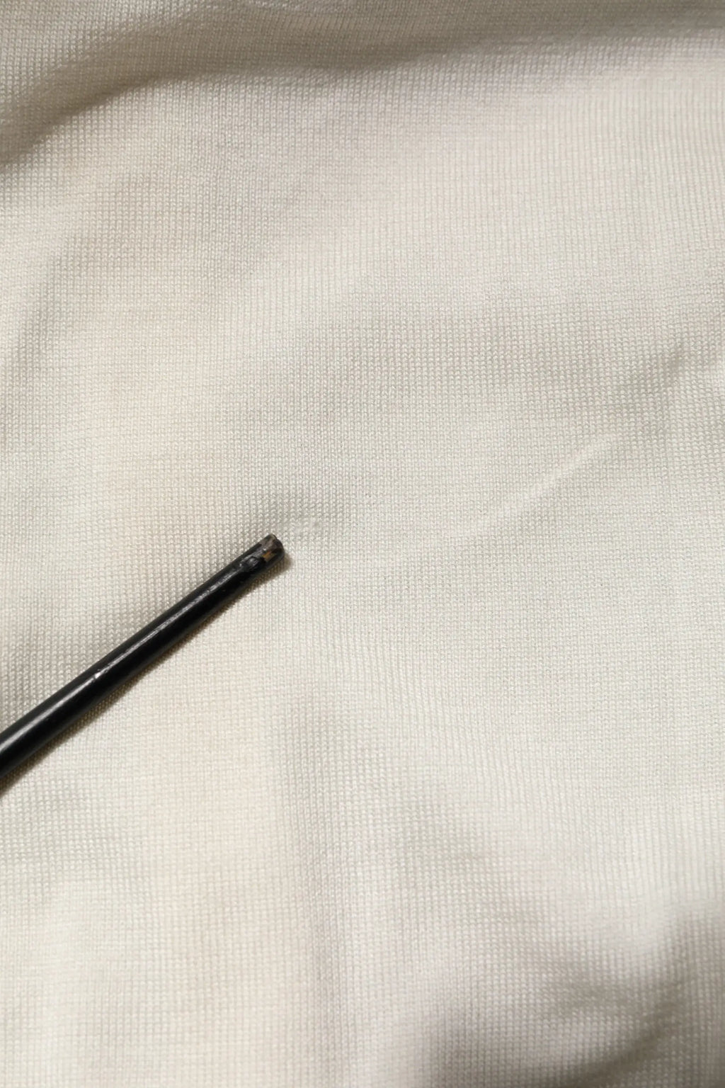 Un tige métallique noire fine avec une pointe légèrement usée repose sur un cardigan dolce & gabbana en soie blanche orné de lys