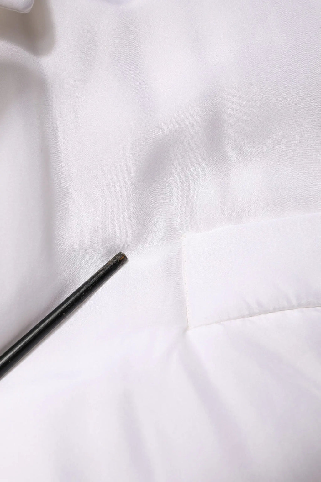 Un repose-baguettes noir élégant posé en diagonale sur un tissu matelassé blanc doux du manteau dolce & gabbana en soie blanche