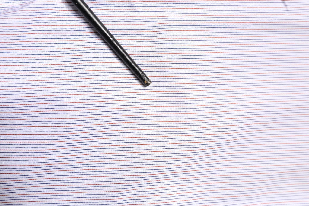 Un stylo noir posé en diagonale sur un tissu rayé bleu marine et rose clair du chemisier Dolce & Gabbana blanc à manches longues