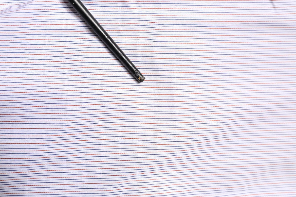 Un stylo noir posé en diagonale sur un tissu rayé bleu marine et rose clair du chemisier Dolce & Gabbana blanc à manches longues