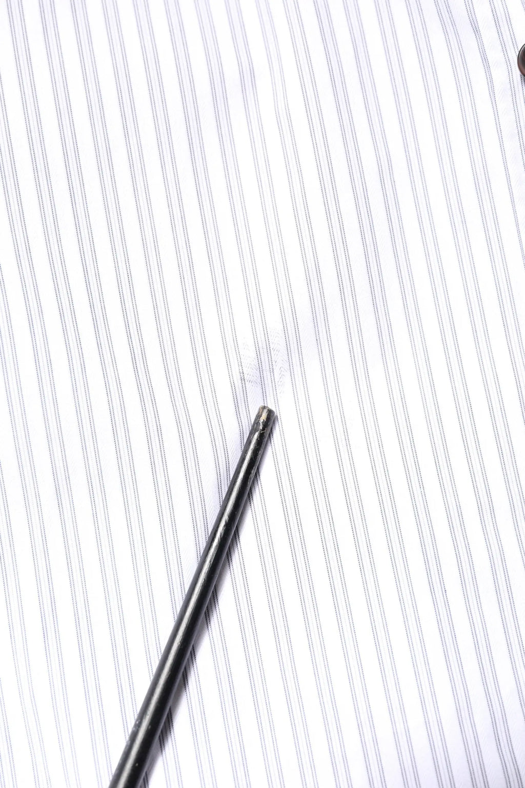 A sleek metallic needle rests diagonally on a dolce & gabbana white striped cotton martini men dress shirt