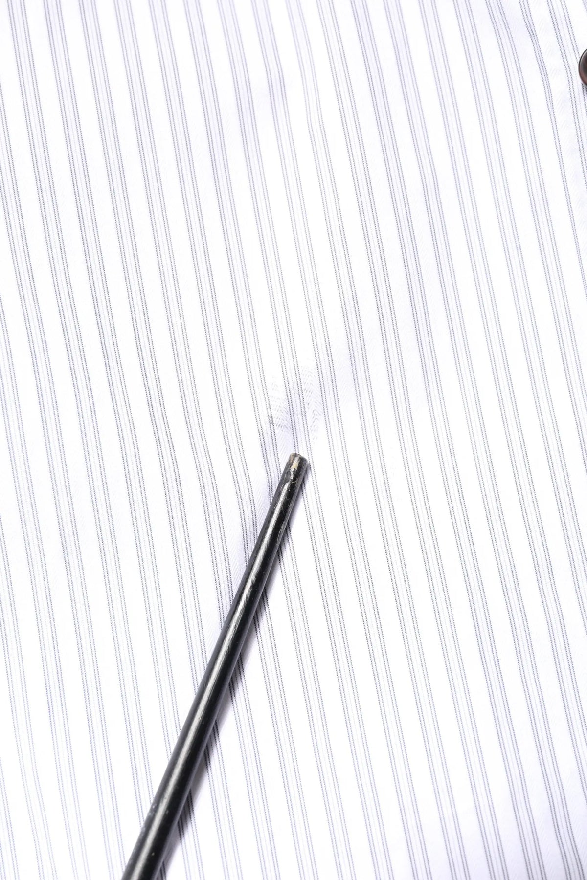 A sleek metallic needle rests diagonally on a dolce & gabbana white striped cotton martini men dress shirt