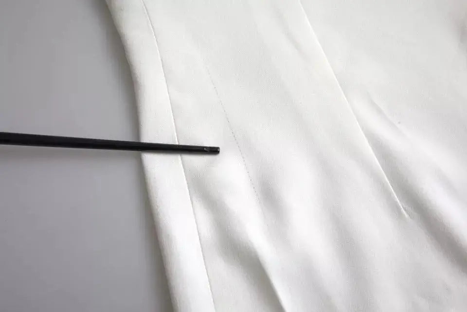 Un repose-baguettes noir élégant posé sur un tissu blanc lisse à côté d’un top blanc en viscose dolce & gabbana manches courtes