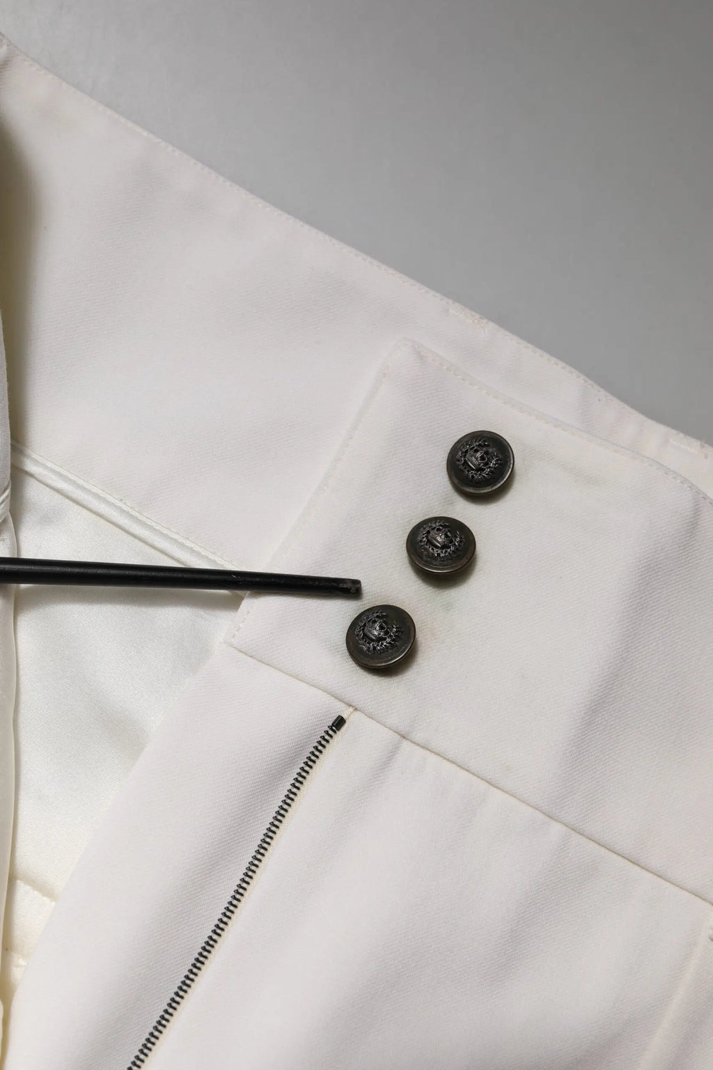 Trois boutons sombres circulaires embossés alignés verticalement sur un panneau de tissu blanc des pantalons dolce & gabbana en laine blanche taille haute fuselés