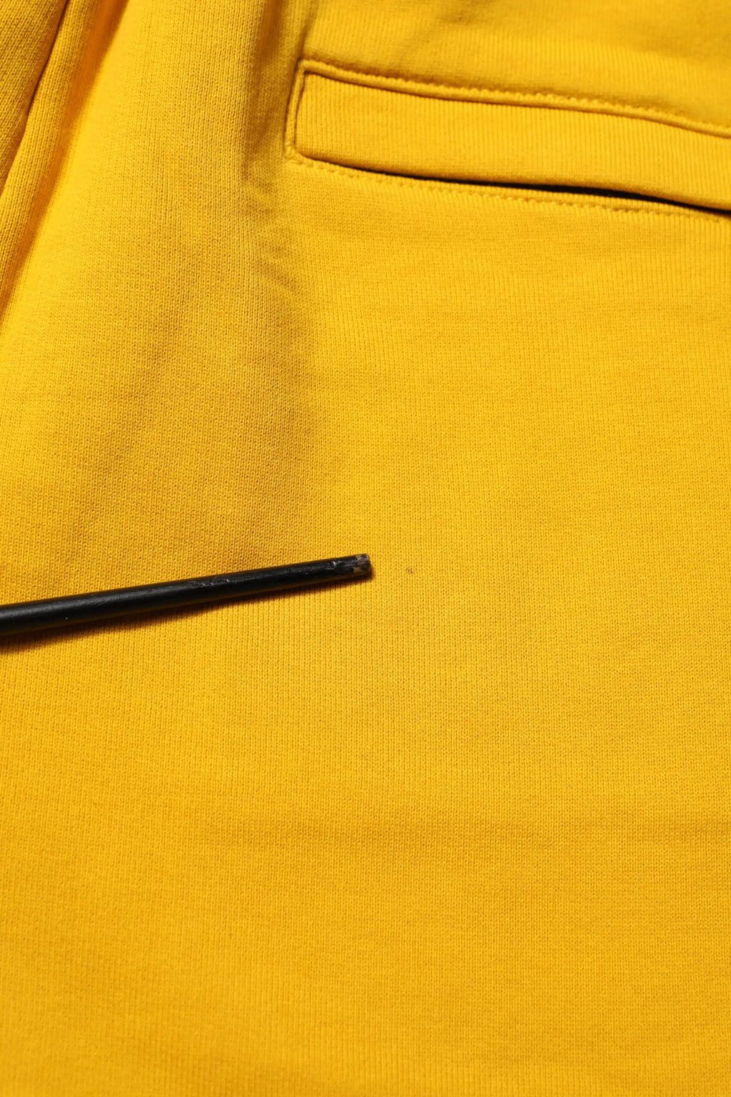 Un crayon noir fin repose sur un tissu jaune vif des pantalons joggers en coton dolce & gabbana