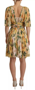 Une femme porte une robe midi plissée dolce & gabbana à imprimé floral jaune vert et rose doux