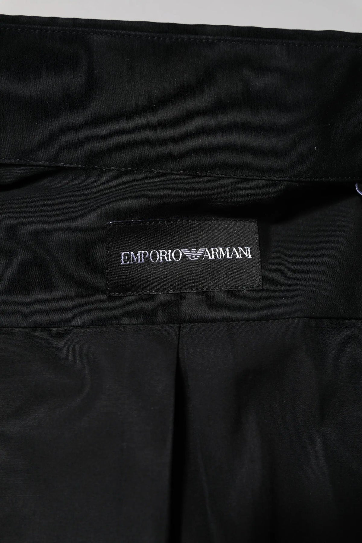 Étiquette noire emporio armani avec logo blanc brodé sur tissu noir pour chemise habillée homme coton manches longues