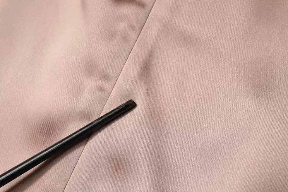 Un repose-baguettes noir élégant posé en diagonale sur un tissu satin blush rose de la robe mini enveloppante emporio armani