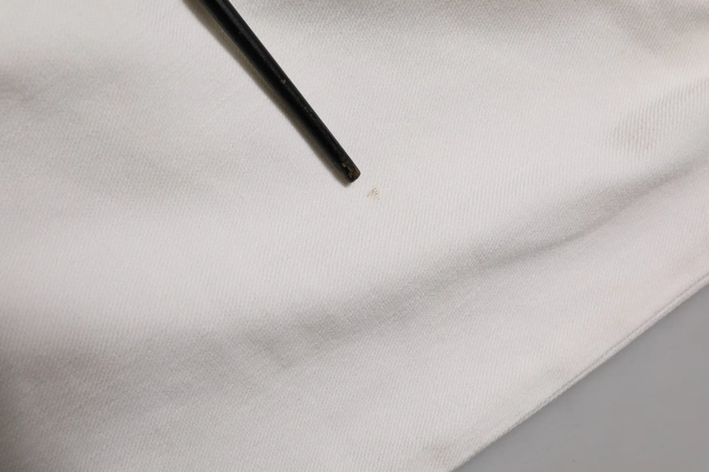 Un crayon noir posé en diagonale sur un tissu blanc lisse près d un pantalon en denim blanc prada taille mi haute ajusté