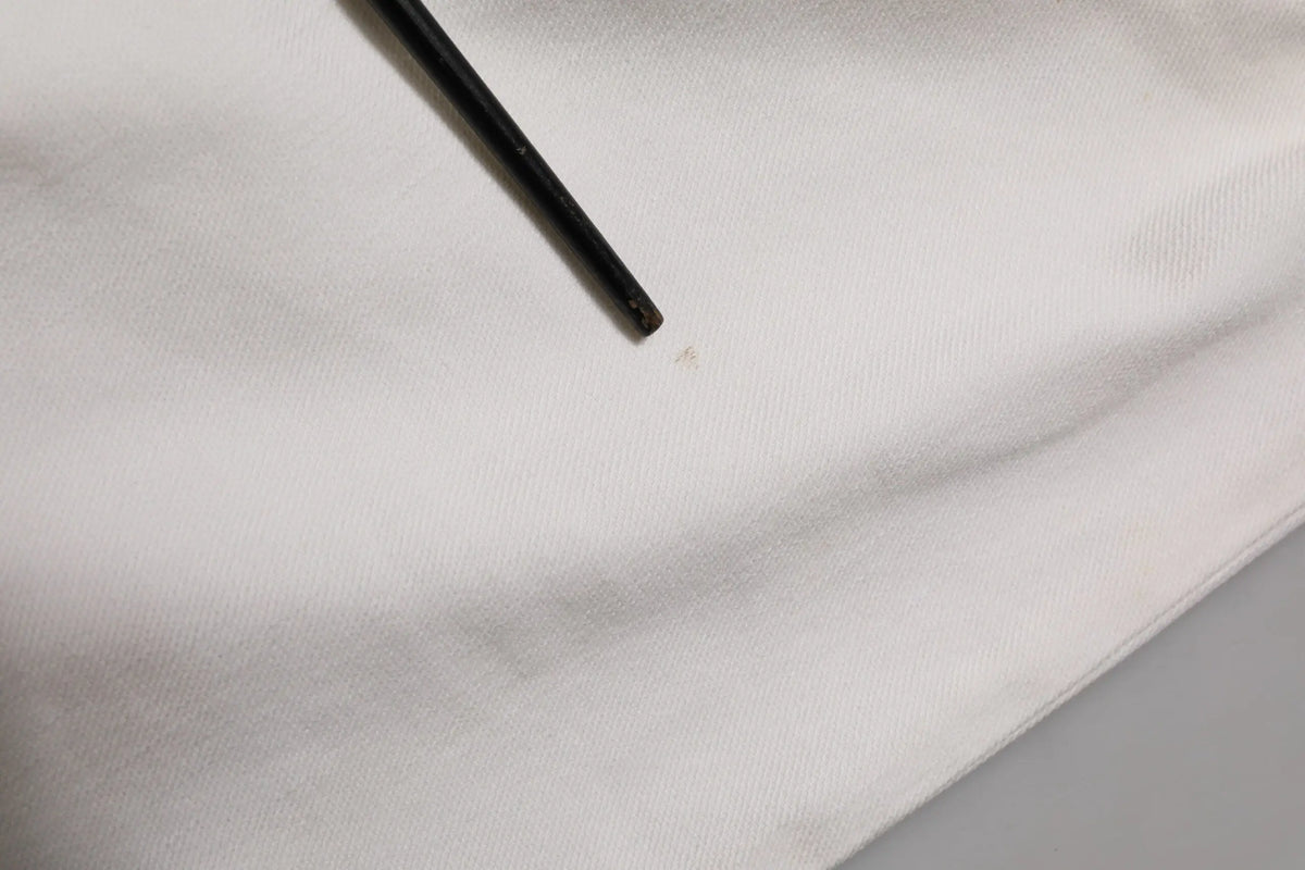 Un crayon noir posé en diagonale sur un tissu blanc lisse près d un pantalon en denim blanc prada taille mi haute ajusté