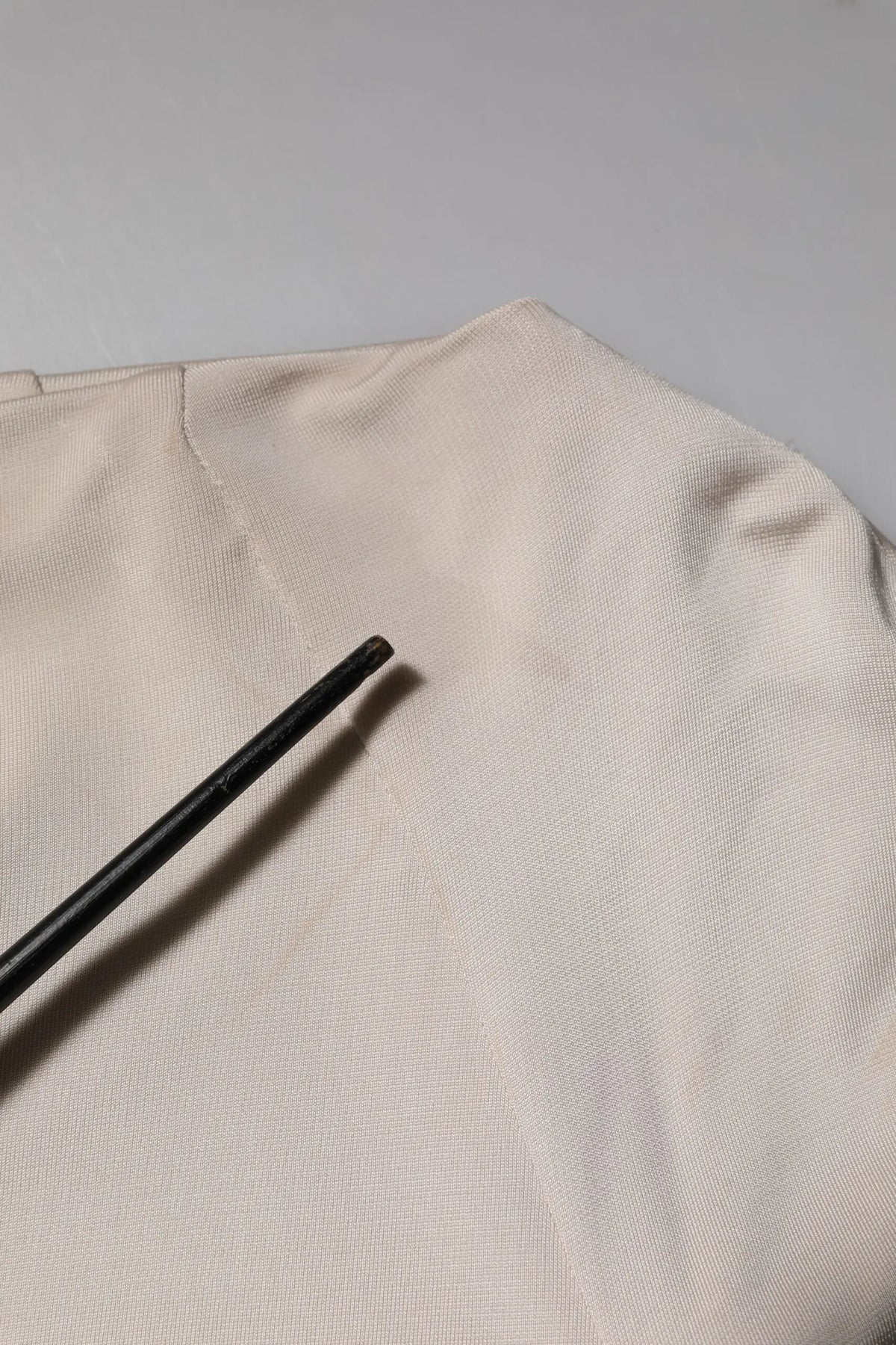 Une paire de baguettes noires élégantes posée en diagonale sur un tissu ivoire texturé avec une robe droite viscose roberto cavalli au genou